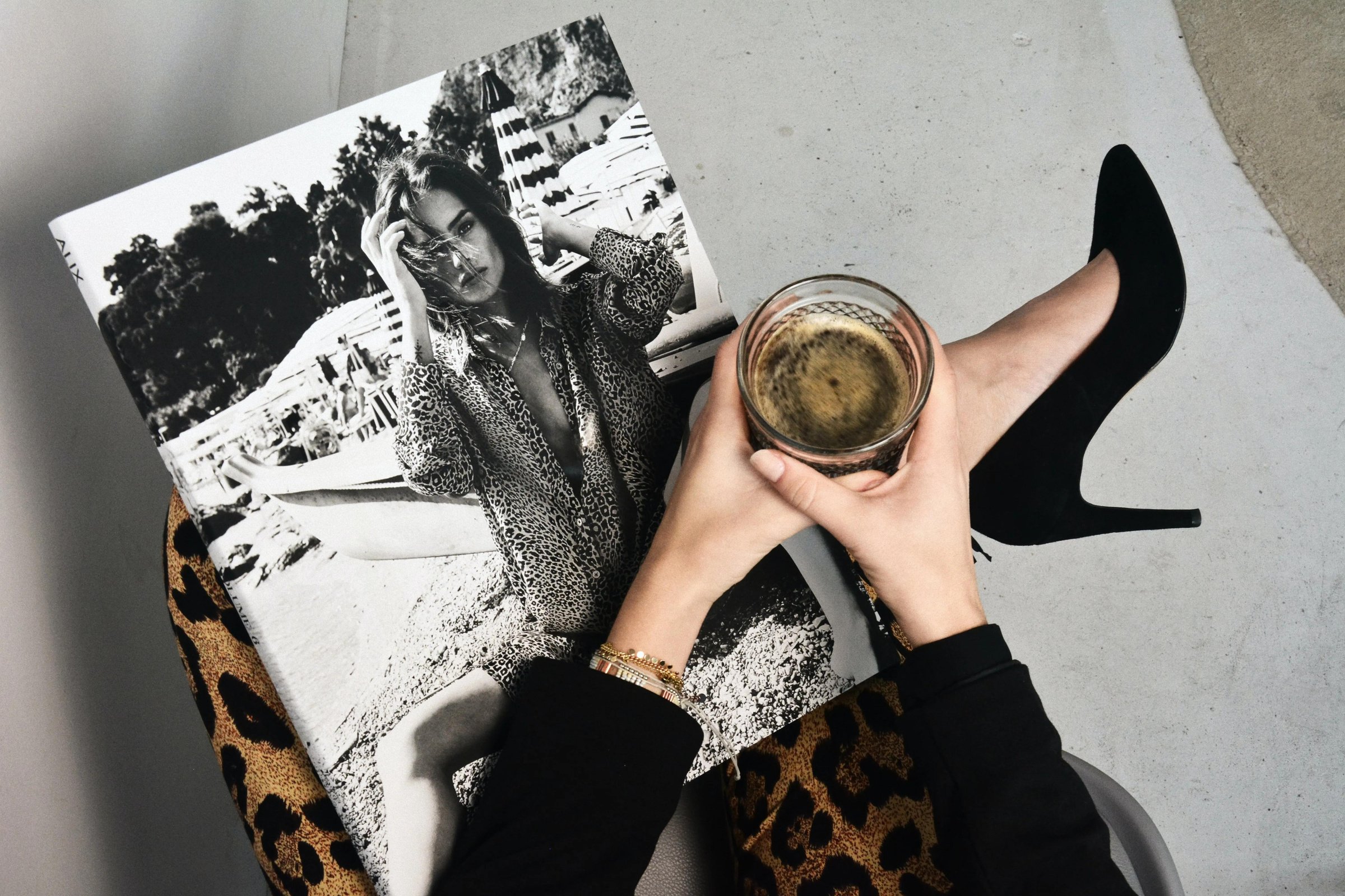 a person in leopard print leggings and high heels holding a cup of coffee with a fashion magazine open