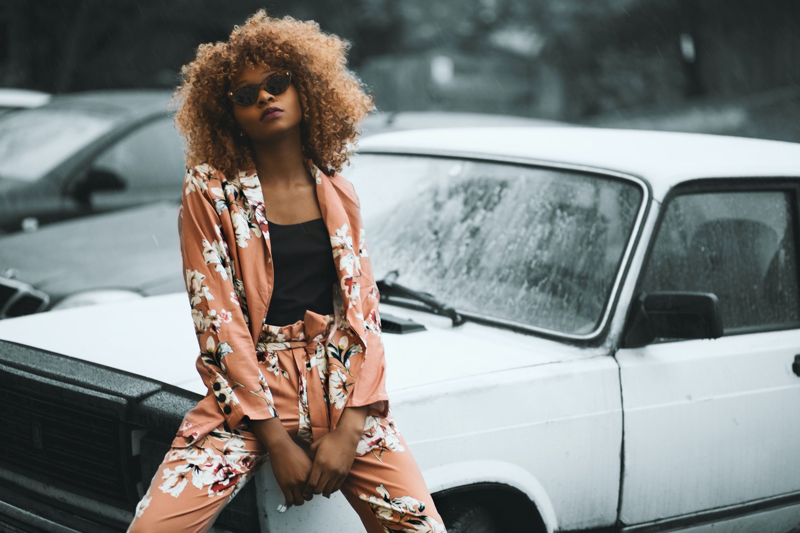 an individual in a floral suit sitting on the hood of a car