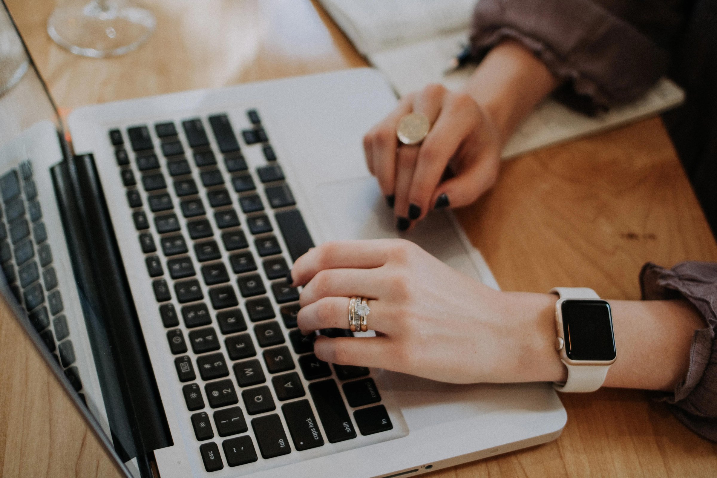 a woman typing on a laptop with a watch on their wrist and rings on her fingers